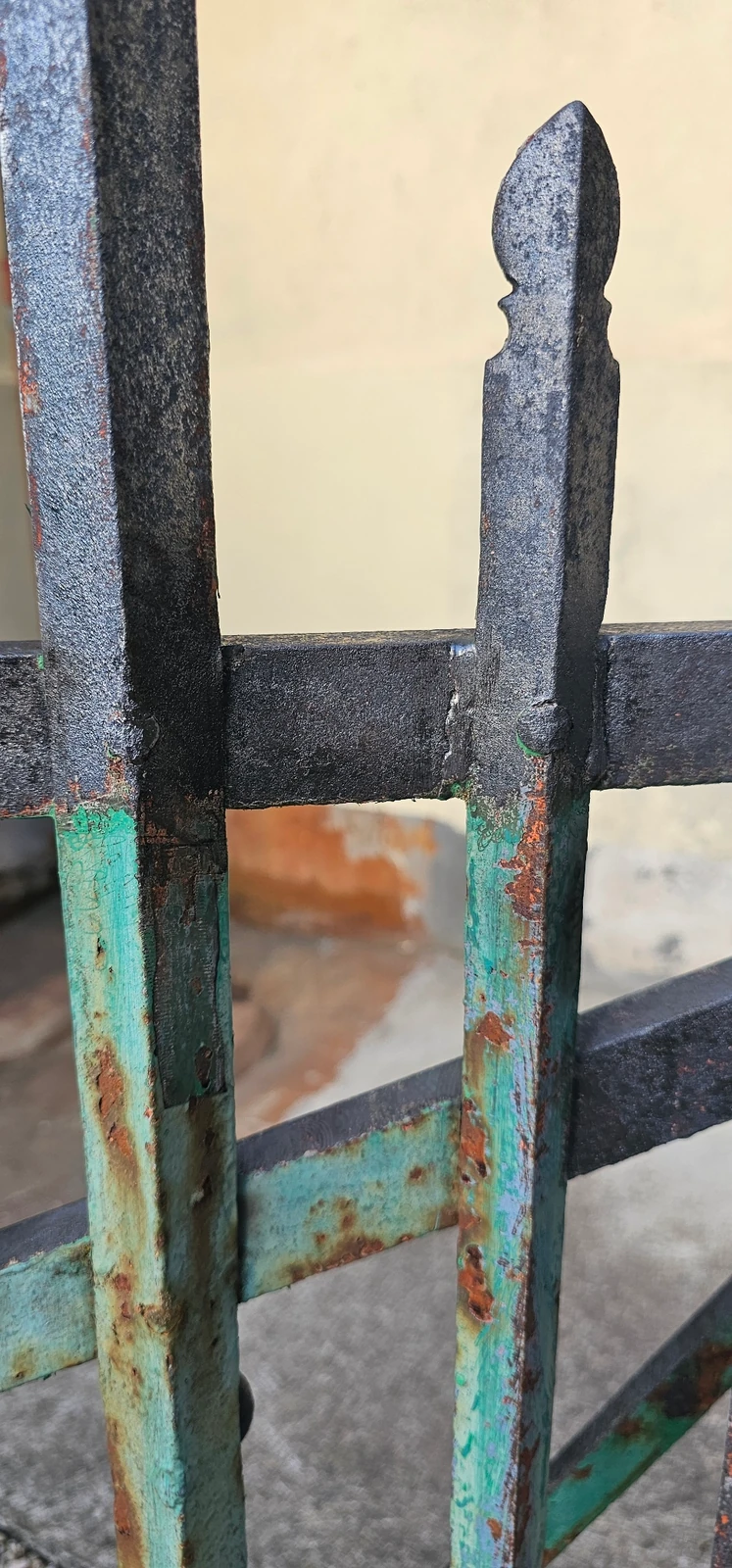 Détail du portail avec peinture verte sur la partie basse et zones décapées au-dessus.
